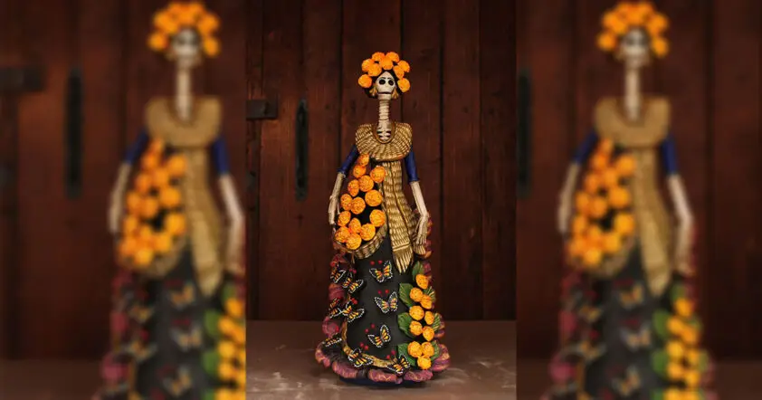 Catrina artesanal de barro decorada con flores de cempasúchil y mariposas monarca, símbolo de la tradición michoacana